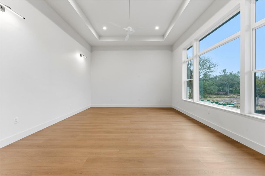 Empty room featuring light wood finished floors, a tray ceiling, a ceiling fan, and recessed lighting