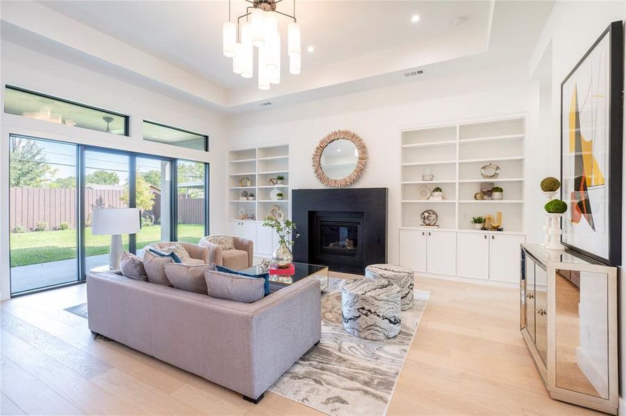 Living room featuring light hardwood / wood-style floors, a raised ceiling, built in features, and an inviting chandelier