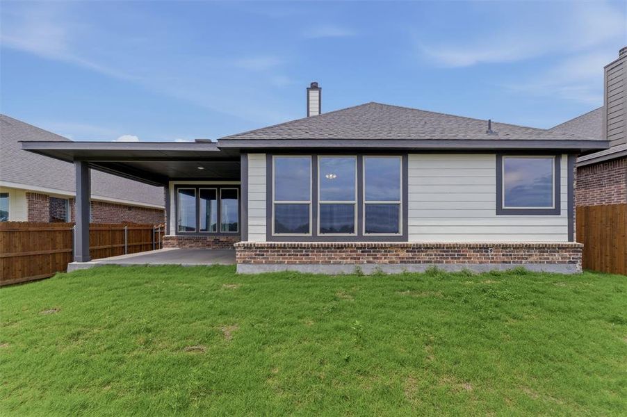 Expansive green lawn backing to a home featuring a covered patio, multiple windows, and a brick foundation Expansive green lawn backing to a home featuring a covered patio, multiple windows, and a brick foundation