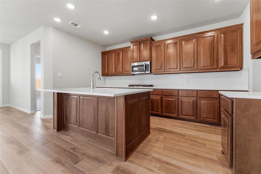 Kitchen with wood finish cabinetry, light wood-style flooring, recessed lighting, a center island with sink, and backsplash
