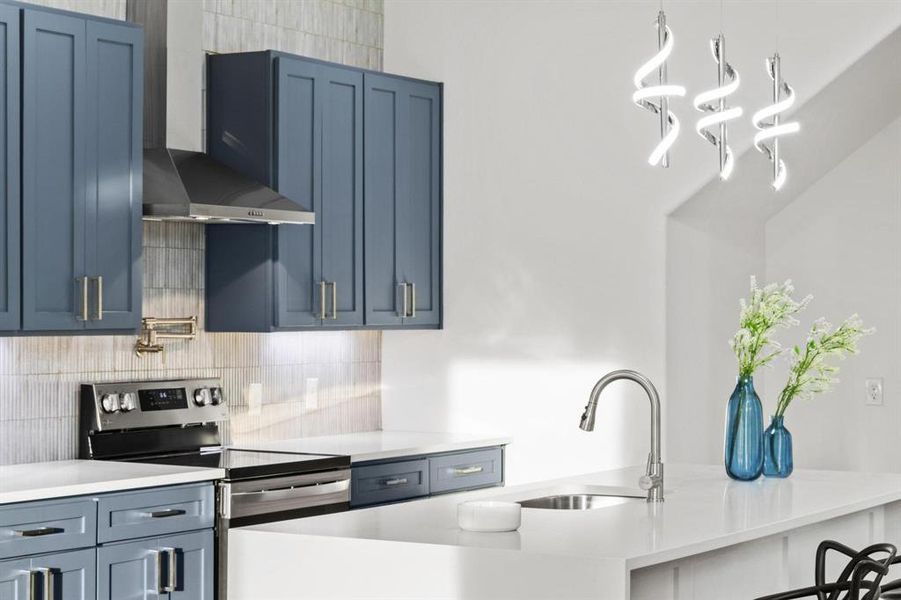 Kitchen with electric stove, wall chimney exhaust hood, hanging light fixtures, a breakfast bar area, and blue cabinets