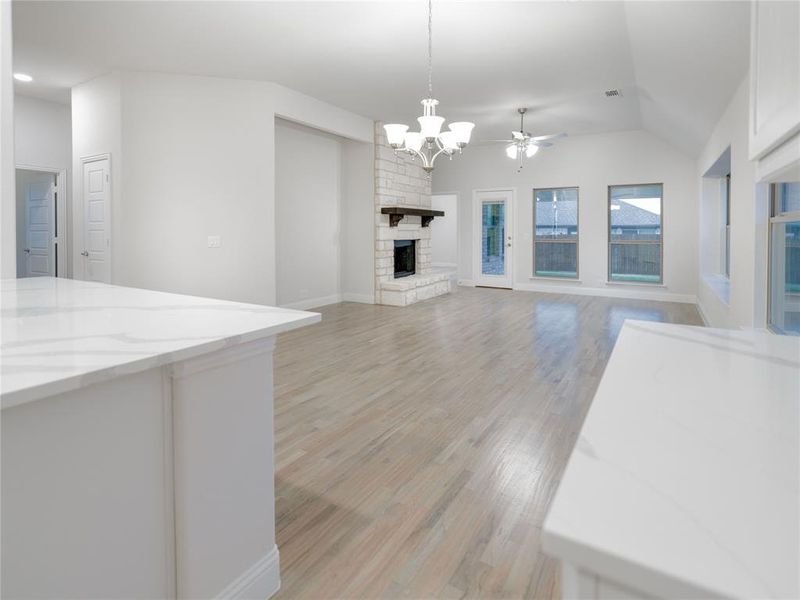 Unfurnished living room featuring lofted ceiling, a fireplace, ceiling fan with notable chandelier, and light hardwood / wood-style flooring