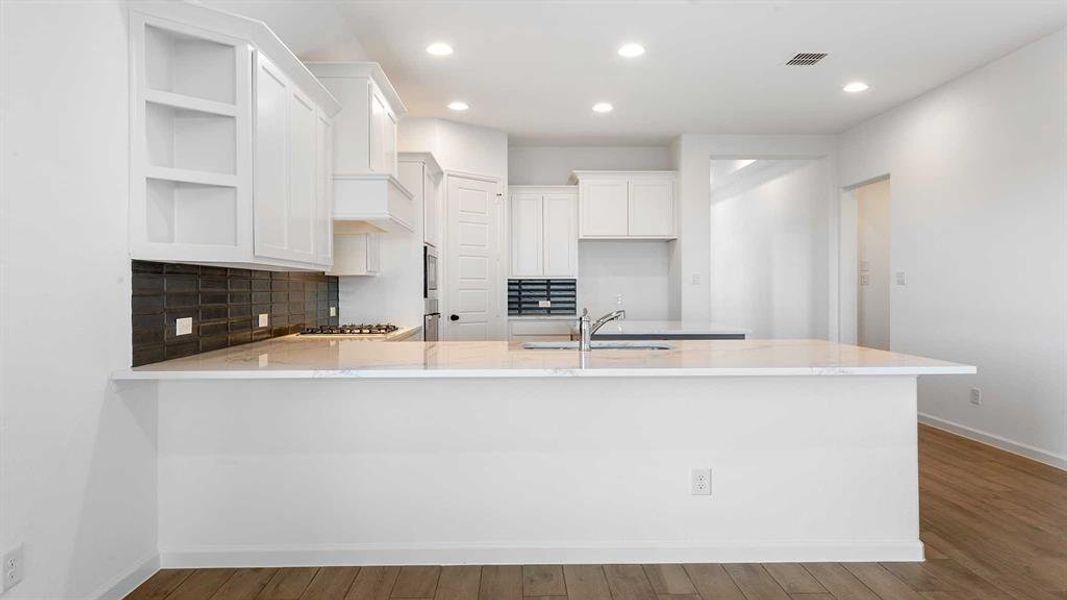 Kitchen with white cabinetry, sink, stainless steel gas cooktop, kitchen peninsula, and hardwood / wood-style flooring