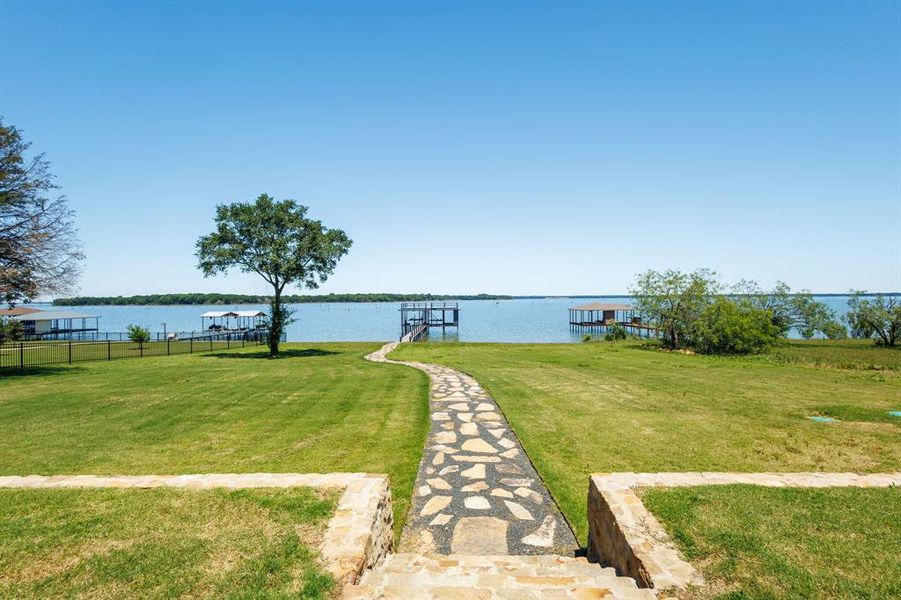 Expansive waterfront grounds featuring a stone pathway, mature trees, and multiple private boat docks