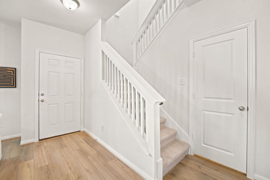 Smooth wood-look flooring and a crisp white staircase create a welcoming entryway.