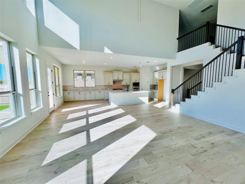 Unfurnished living room featuring a towering ceiling, stairway, a skylight, light wood-style flooring, and recessed lighting