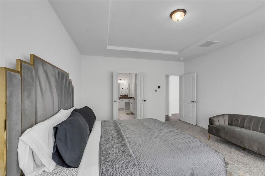 Bedroom with carpet flooring, a raised ceiling, and ensuite bath