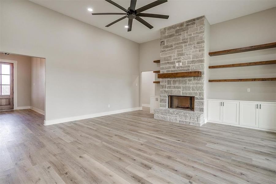 Living room featuring light wood-type flooring, a fireplace, ceiling fan, and high ceilings