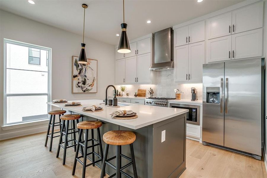 Kitchen featuring stainless steel fridge, backsplash, white cabinetry, a kitchen bar, and pendant lighting Kitchen featuring stainless steel fridge, backsplash, white cabinetry, a kitchen bar, and pendant lighting