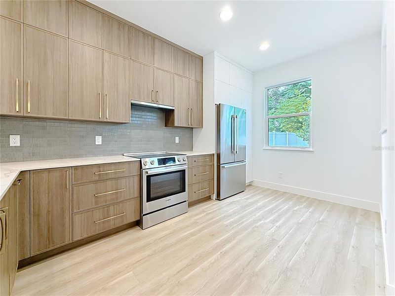 Sleek and modern kitchen featuring custom wood cabinetry, quartz waterfall countertops, stainless steel appliances, and stylish accent details — all bathed in natural light. Sleek and modern kitchen featuring custom wood cabinetry, quartz waterfall countertops, stainless steel appliances, and stylish accent details — all bathed in natural light.