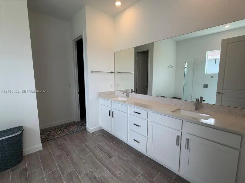 Dual-vanity cabinet with light-toned solid surface countertops, rectangular undermount sinks, wood-finish tile flooring, and wall-to-wall mirror