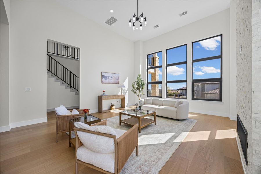 Living area with light wood-type flooring, a fireplace, a high ceiling, and a chandelier