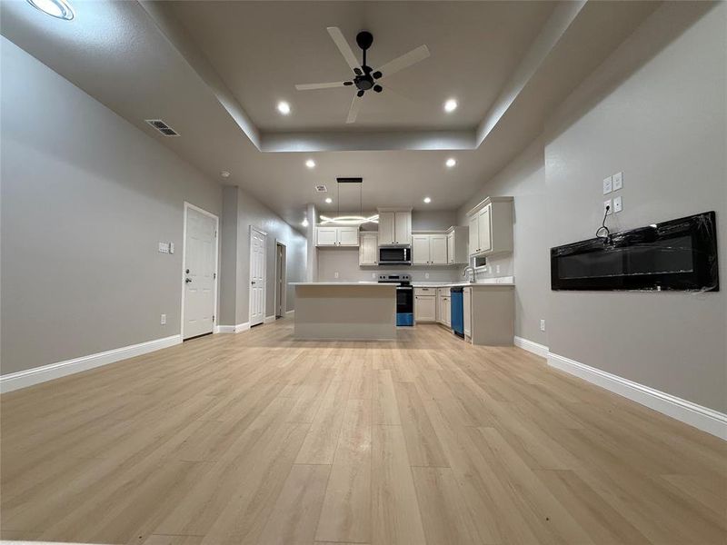 Unfurnished living room with light wood-style flooring, recessed lighting, a ceiling fan, and a tray ceiling