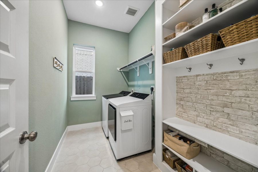 The spacious laundry room features built-in shelving above the washer and dryer along with a floor-to-ceiling mudroom organizer complete with hooks and multiple storage cubbies for everyday convenience.