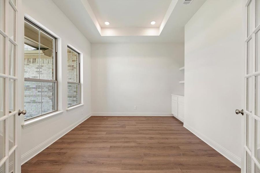 Empty room with dark wood-type flooring, a tray ceiling, and french doors