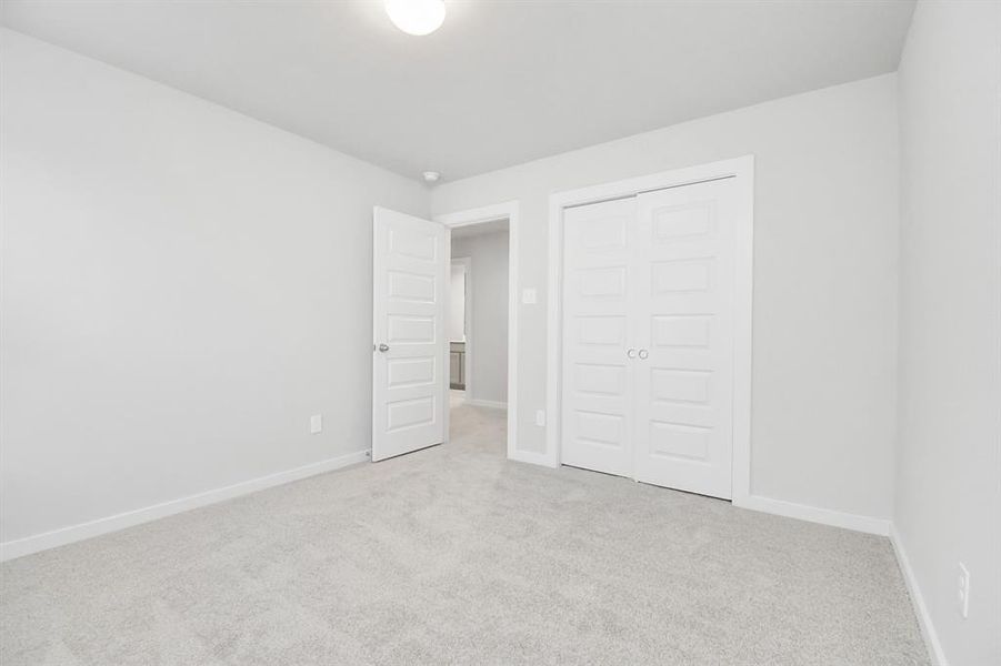 A cozy secondary bedroom with large windows, plush carpet, and spacious closets. The natural light and neutral colors create a serene, inviting atmosphere.