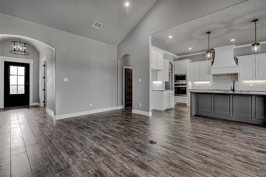 Kitchen featuring decorative light fixtures, premium range hood, light stone countertops, stainless steel appliances, and white cabinets