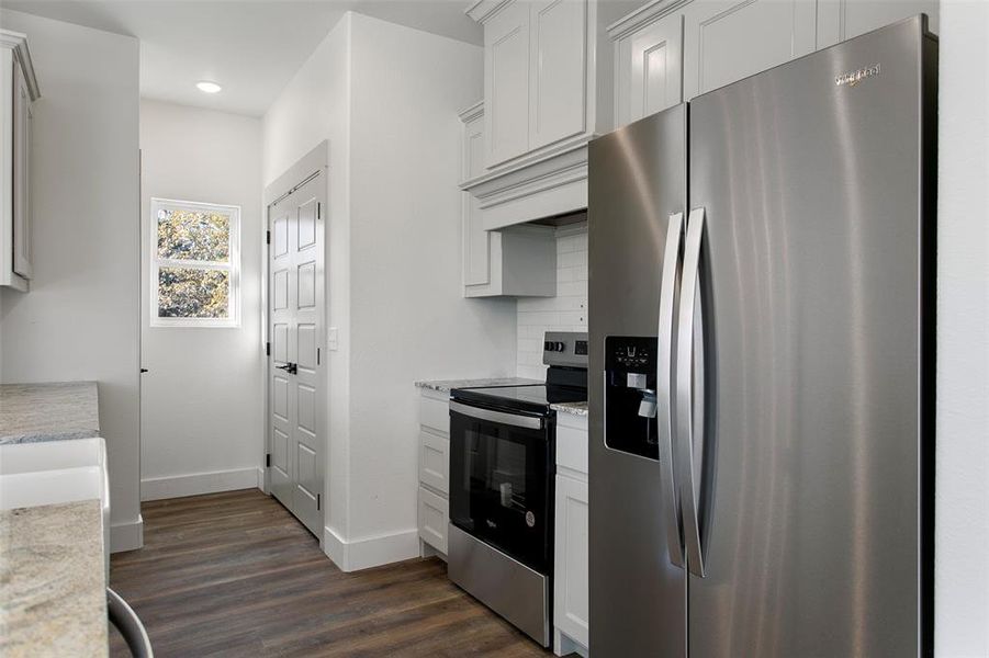 Kitchen featuring white cabinets, dark hardwood / wood-style flooring, backsplash, and appliances with stainless steel finishes