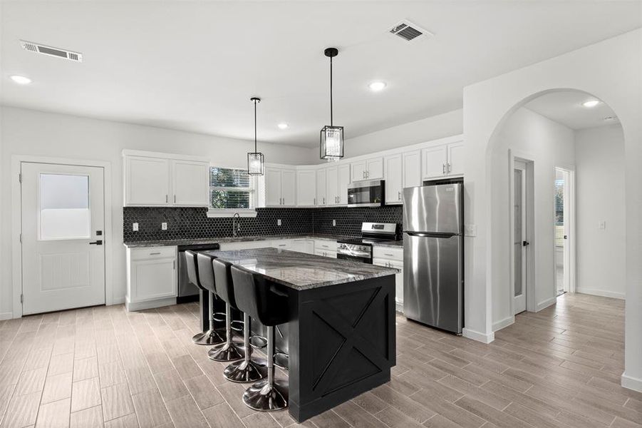 Kitchen with a kitchen bar, stainless steel appliances, white cabinetry, dark stone countertops, and recessed lighting
