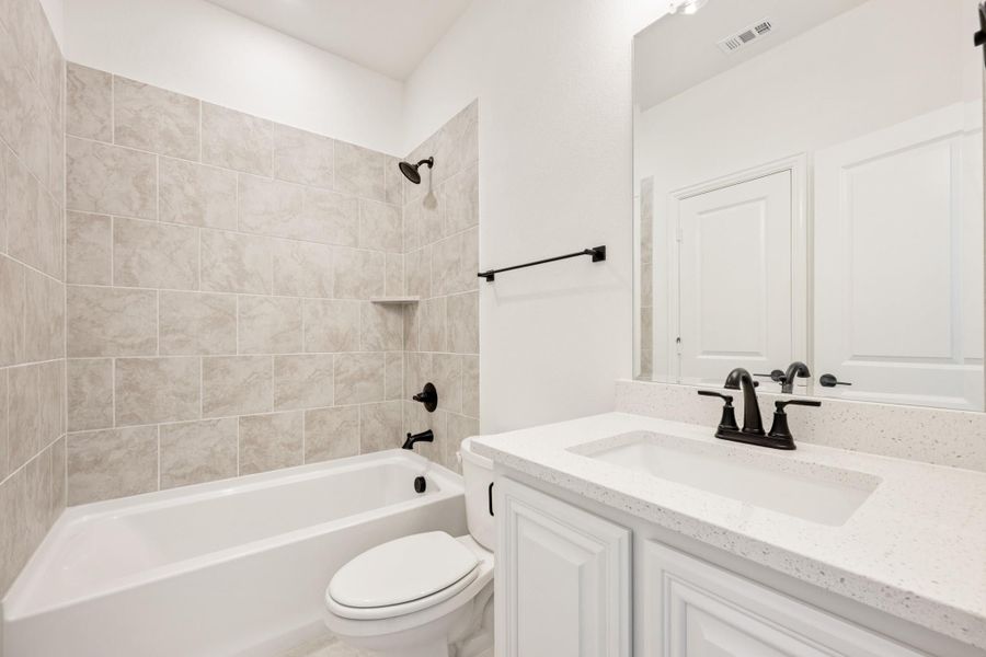 Bathroom with tiled tub-shower combo, white vanity with quartz countertop, and black fixtures