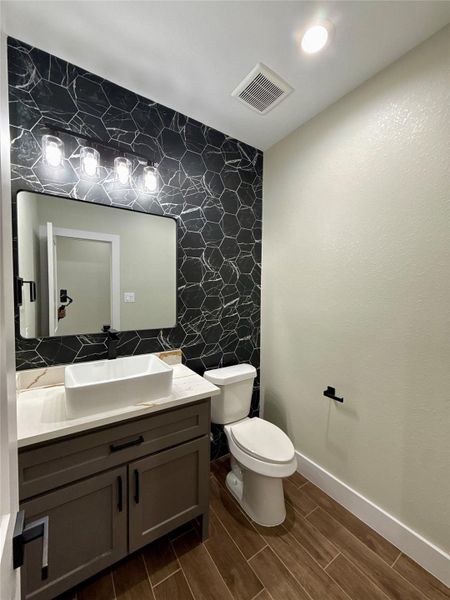 Modern bathroom featuring a stylish black hexagonal accent wall, a sleek vessel sink on a gray vanity, and wood-look tile flooring. Bright lighting and a neutral color palette create a clean, contemporary feel. Modern bathroom featuring a stylish black hexagonal accent wall, a sleek vessel sink on a gray vanity, and wood-look tile flooring. Bright lighting and a neutral color palette create a clean, contemporary feel.