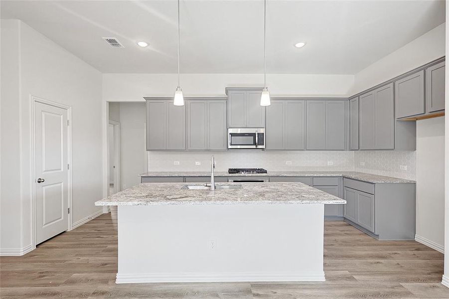 Kitchen featuring a center island with sink, pendant lighting, and light wood-type flooring