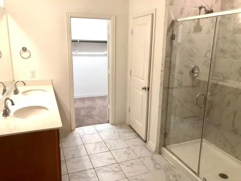 Full bathroom featuring light marble finish flooring, a stall shower, double vanity, and a spacious closet Full bathroom featuring light marble finish flooring, a stall shower, double vanity, and a spacious closet