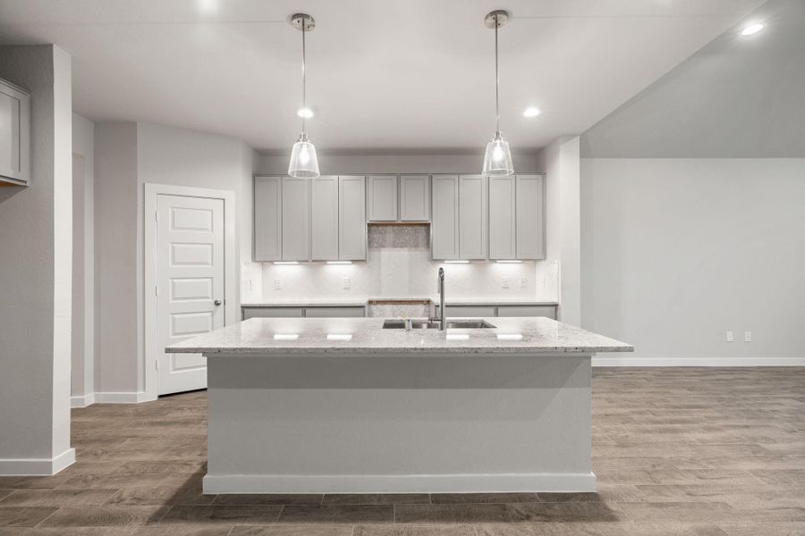 Culinary haven, featuring granite countertops, a tile backsplash, stainless steel appliances, 42” upper cabinets, and undercabinet lighting. Sample photo of completed home with similar floor plan. As-built interior colors and selections may vary.