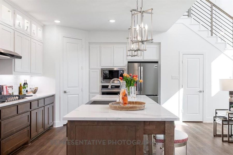 Kitchen featuring an island with sink, hanging light fixtures, dark wood-style flooring, white cabinets, and stainless steel appliances
