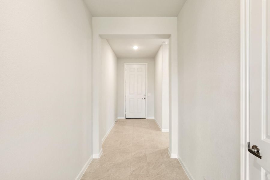 Narrow hallway with white walls, tile floors, and a white paneled door at the end