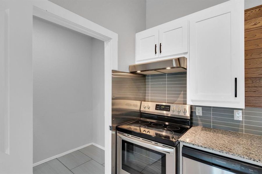 Kitchen featuring under cabinet range hood, stainless steel appliances, light stone counters, tasteful backsplash, and white cabinets