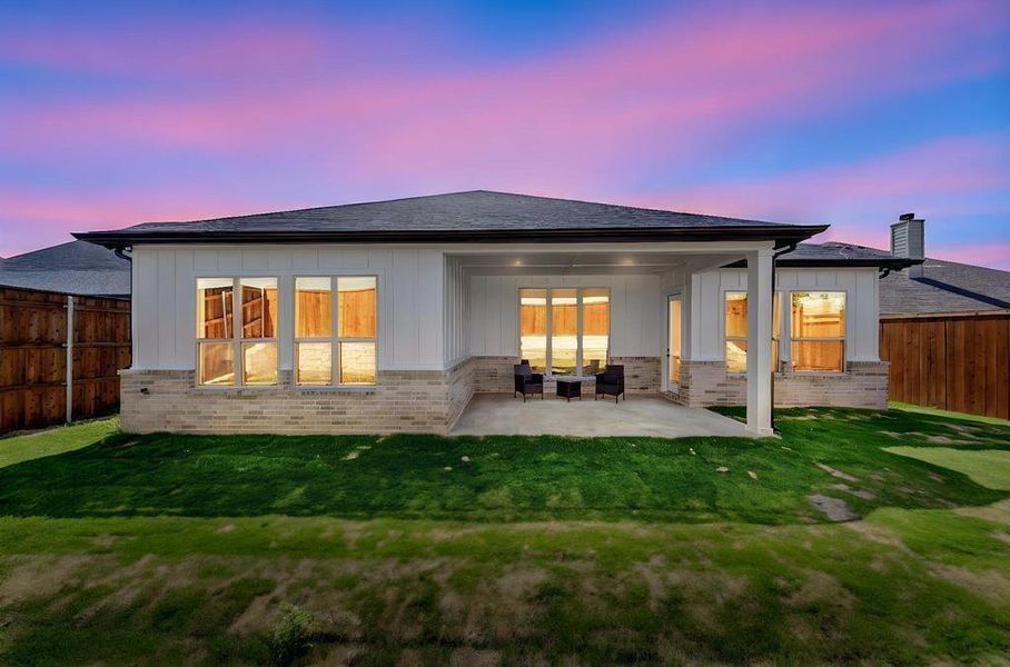 Back of house at dusk featuring board and batten siding, brick siding, a patio area, and a fenced backyard