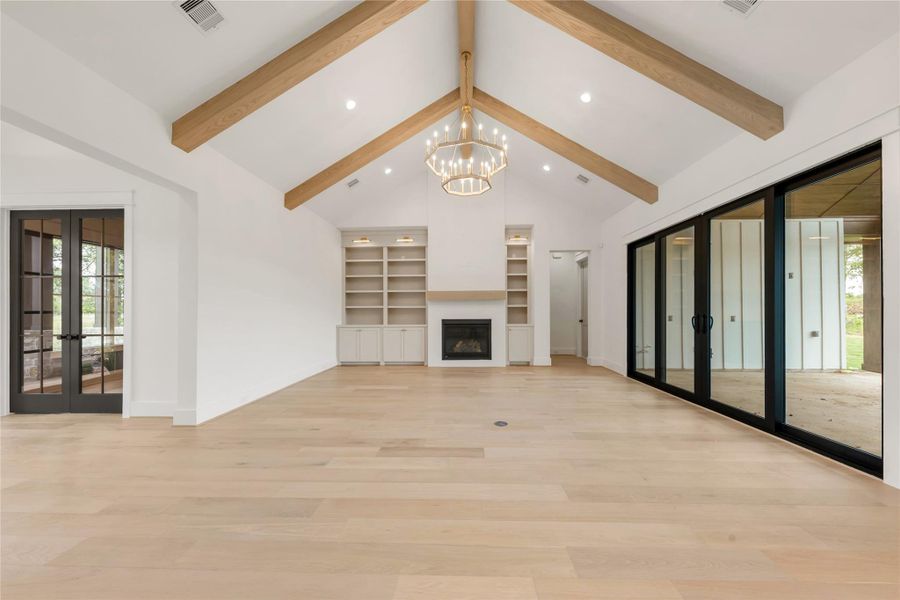 Unfurnished living room featuring french doors, healthy amount of natural light, light wood finished floors, and a chandelier