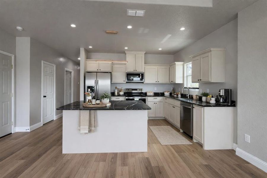 Kitchen featuring stainless steel appliances, light wood finished floors, dark stone countertops, a center island, and white cabinetry