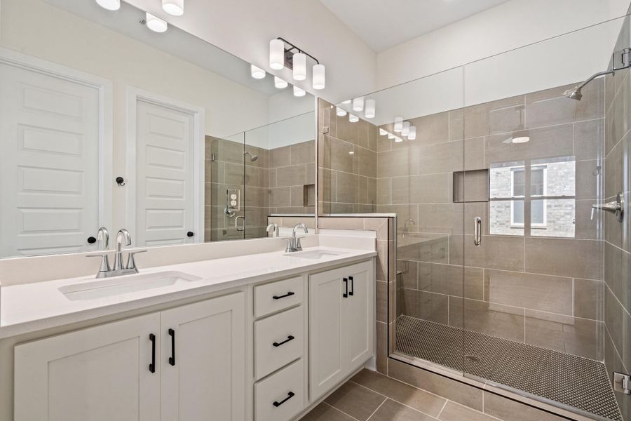 Bathroom featuring double vanity, a shower stall, and light tile patterned floors