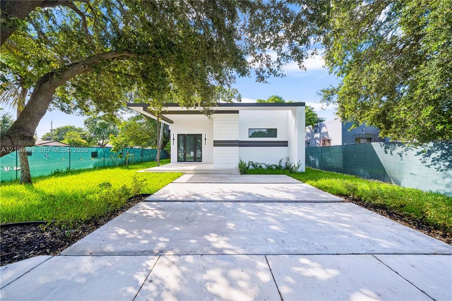 Modern exterior featuring clean lines, a flat roofline, minimalist facade detailing, a paved concrete driveway, and mature landscaping Modern exterior featuring clean lines, a flat roofline, minimalist facade detailing, a paved concrete driveway, and mature landscaping