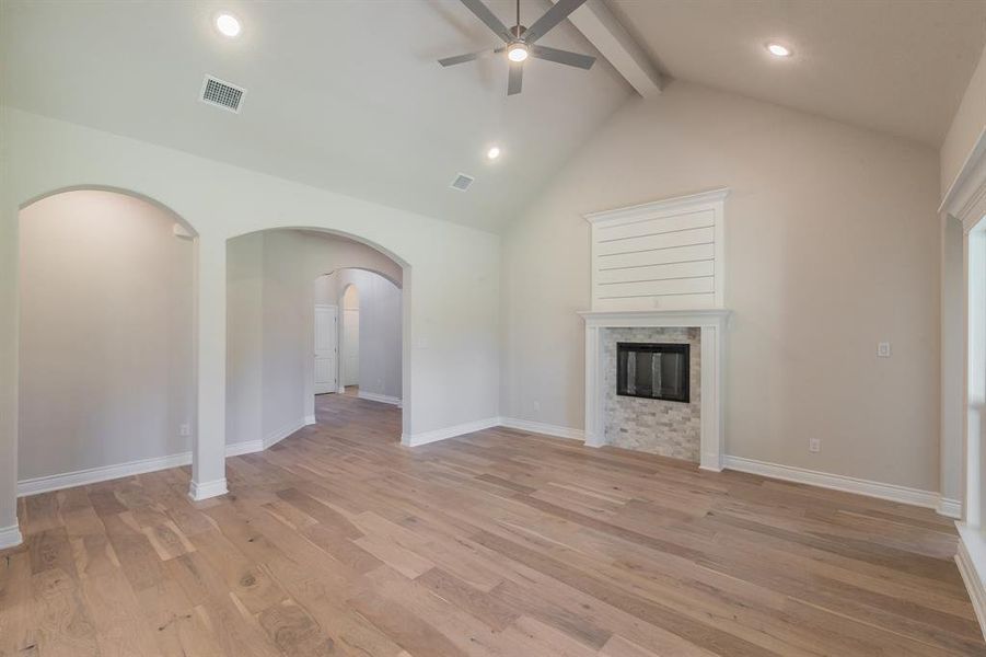 Unfurnished living room featuring beam ceiling, light hardwood / wood-style floors, high vaulted ceiling, and ceiling fan