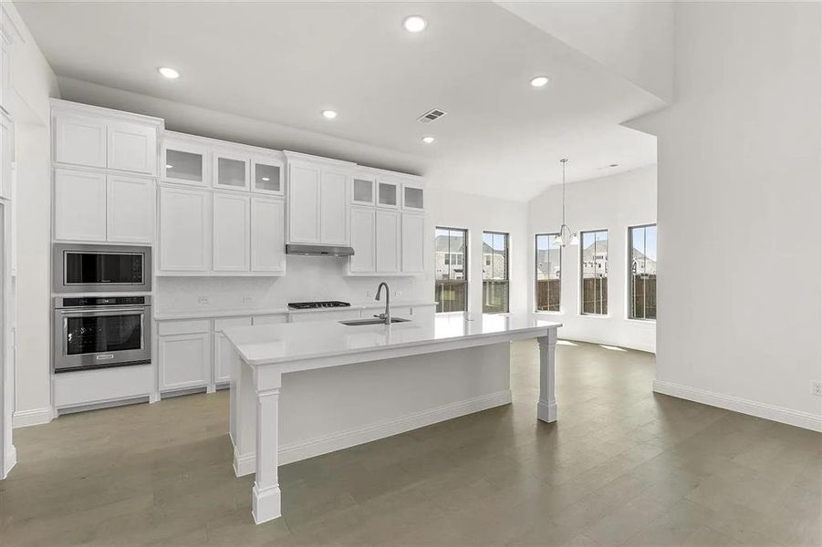 Kitchen featuring white cabinets, stainless steel oven, sink, and an island with sink