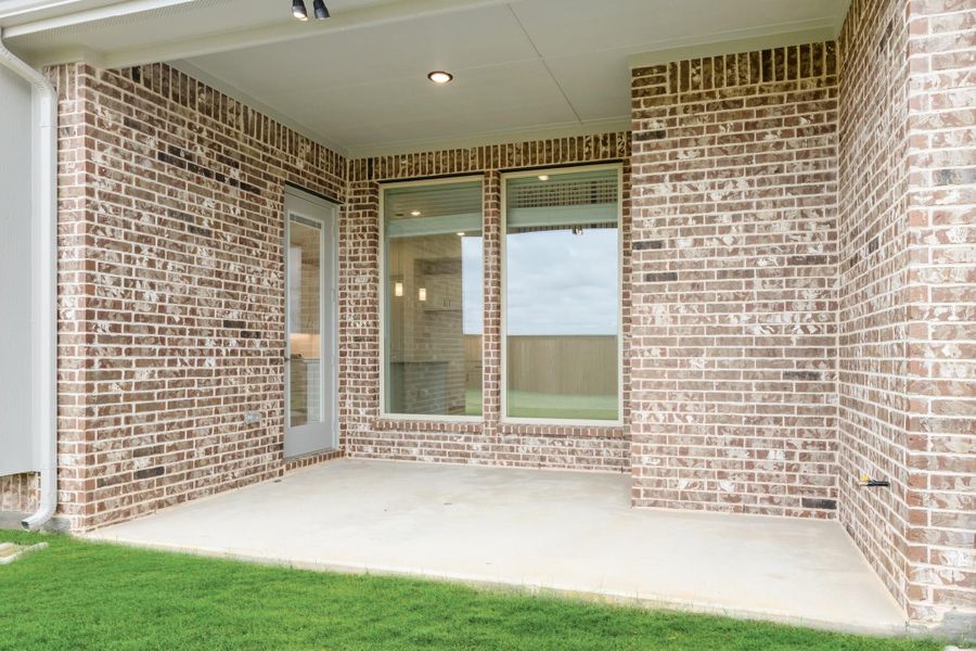 Covered back patio with concrete floor, brick walls, and glass door leading inside