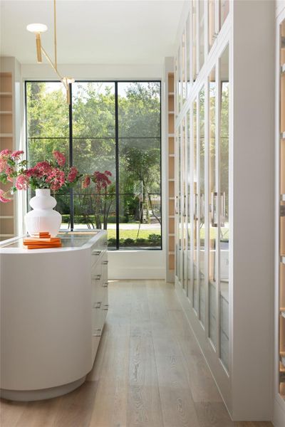 The oversized walk-in closet includes custom built-ins, a center island, glass-front wardrobe doors with integrated lighting, open shelving, shoe racks, and custom drawers and cabinetry. The oversized walk-in closet includes custom built-ins, a center island, glass-front wardrobe doors with integrated lighting, open shelving, shoe racks, and custom drawers and cabinetry.