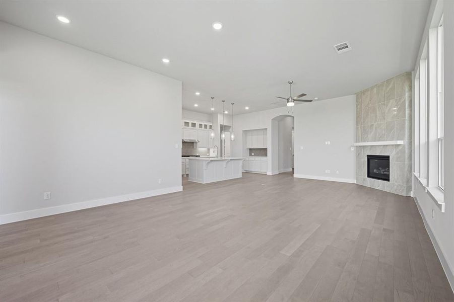 Unfurnished living room featuring arched walkways, a tile fireplace, recessed lighting, ceiling fan, and light wood-style floors Unfurnished living room featuring arched walkways, a tile fireplace, recessed lighting, ceiling fan, and light wood-style floors