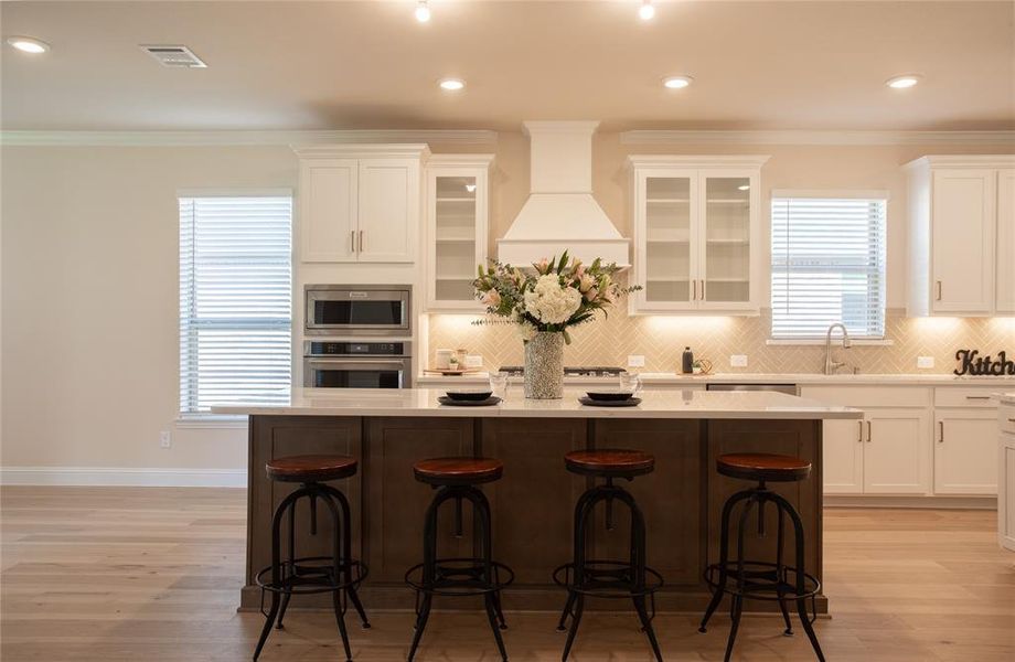 Kitchen with custom range hood, stainless steel appliances, tasteful backsplash, and a kitchen island with sink