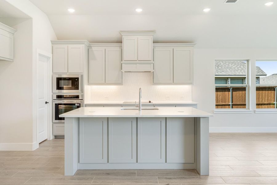Kitchen with large center island, white cabinets, built-in double oven, and light tile floors