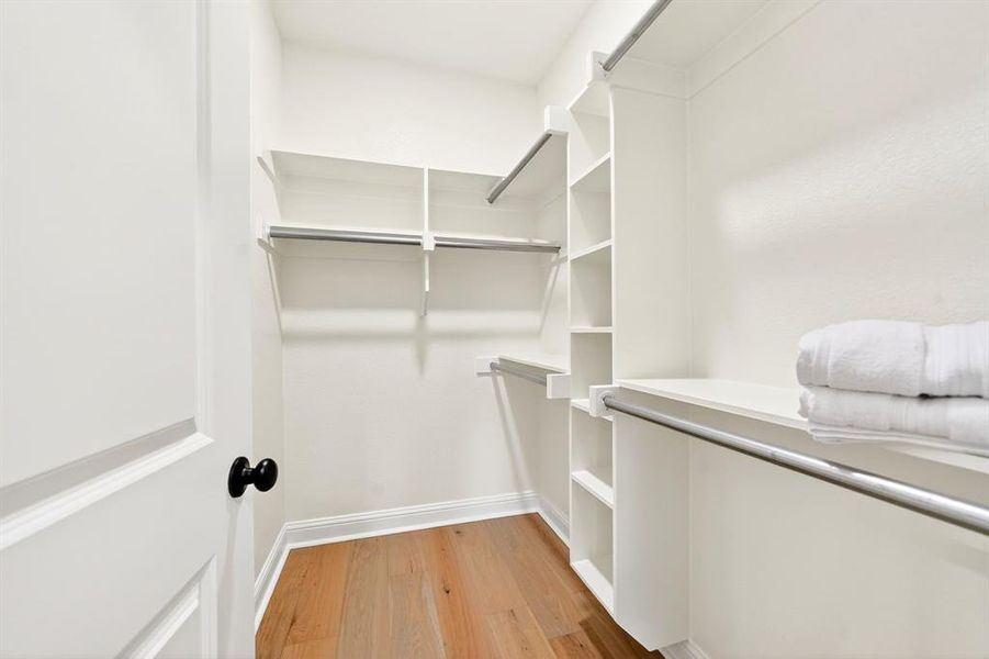 Walk-in closet featuring built-in shelving, multiple hanging rods, wood-finish flooring, and crisp white trim