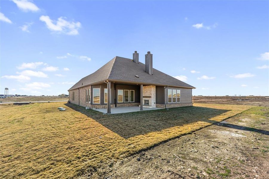 Back of house featuring a patio, a chimney, a yard, brick siding, and stone siding