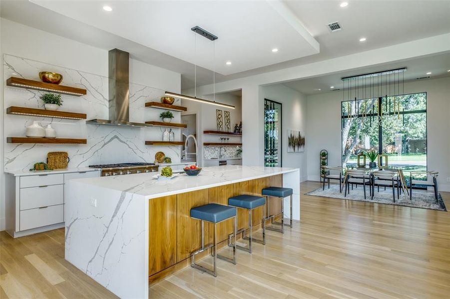 Kitchen with white cabinetry, light hardwood / wood-style flooring, a kitchen bar, island exhaust hood, and a center island with sink