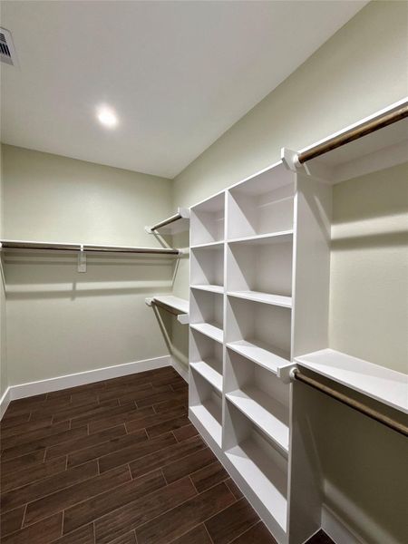 Spacious walk-in closet with ample shelving and hanging space, featuring modern lighting and dark wood tile look flooring. Ideal for organized storage. Spacious walk-in closet with ample shelving and hanging space, featuring modern lighting and dark wood tile look flooring. Ideal for organized storage.