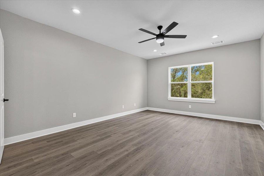 A well-lit bedroom with elegant flooring and a window offering views of mature trees. A well-lit bedroom with elegant flooring and a window offering views of mature trees.