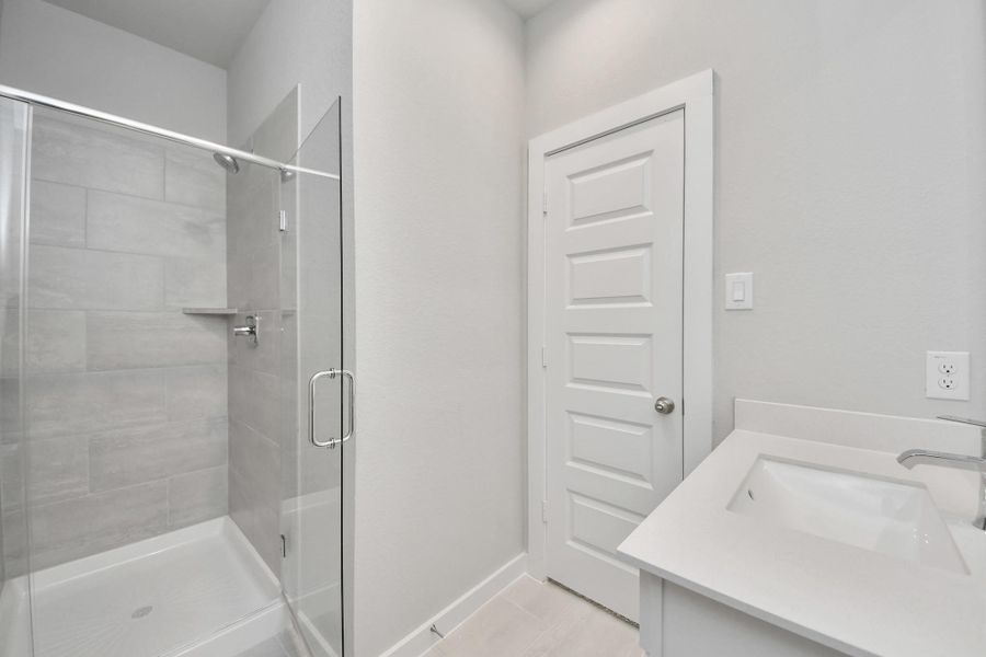 Secondary bath features tile flooring, a walk-in shower with tile surround, light stained wood cabinets, beautiful light countertop. Sample photo of completed home with similar floor plan. Actual colors and selections may vary.