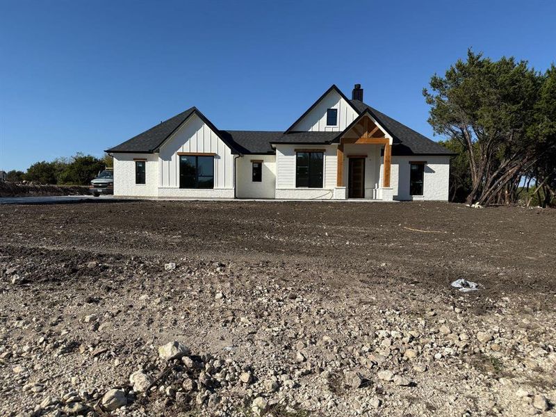 Modern farmhouse featuring a shingled roof, a chimney, and board and batten siding Modern farmhouse featuring a shingled roof, a chimney, and board and batten siding